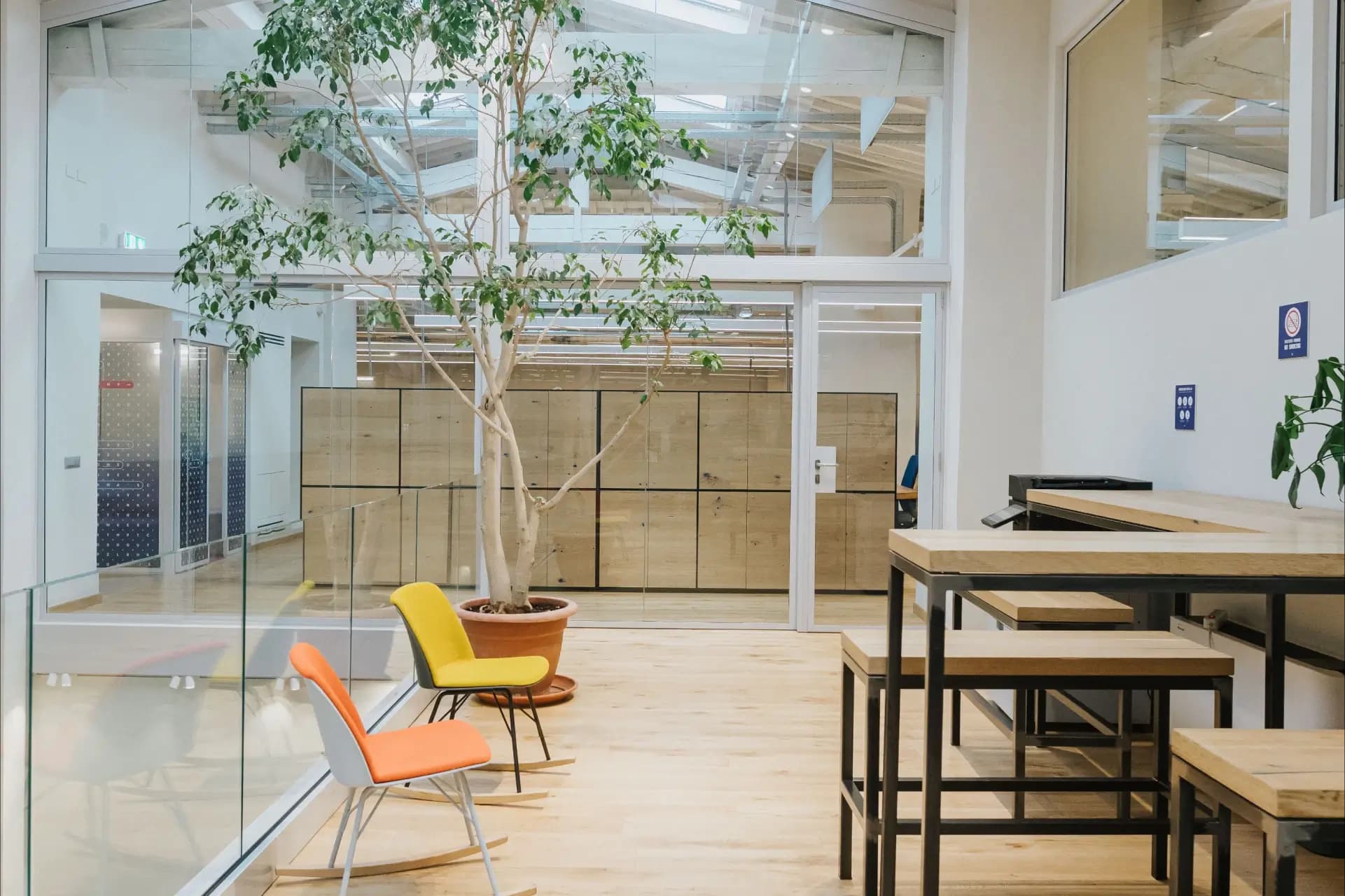 Area coworking di Nana Bianca con postazioni di lavoro elevate, sedute moderne e albero decorativo interno. Un ambiente ispirato alla natura per il massimo comfort lavorativo.